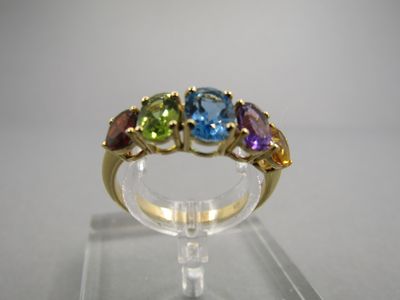 une image d'une bague ornée de pierres multicolores posée sur un socle transparent