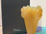 un vase jaune posé sur un sol carrelé, à côté d'une boîte noire