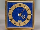a small blue clock with gold hands on a wooden table