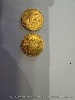 deux pièces d'or posées sur une table blanche, à côté de l'ombre d'une personne