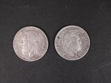 two silver coins sitting side by side on a black surface
