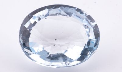 un gros plan d'une topaze bleue facettée posée sur une surface blanche