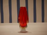 a red vase sitting on a white table with a blue and white striped background