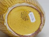 a yellow vase sitting on a white surface with a tag on it