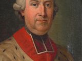 portrait of a man in a red collared shirt with a cross on his chest