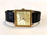une montre en or avec un bracelet en cuir noir posée sur une surface blanche