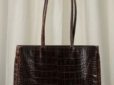 brown alligator skin handbag on a wooden table with curtains in the background