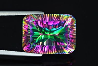 a close up of a square cut rainbow colored diamond on a black surface