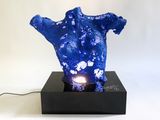 a blue sculpture on a black stand with a light on it