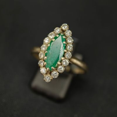 une bague sertie d'une émeraude et de diamants, exposée sur un fond noir