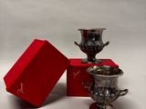 deux tasses en argent posées à côté d'une boîte rouge sur une surface blanche