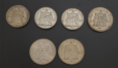 six different types of silver coins on a black surface