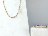 Le collier et le bracelet en chaîne d'or sont exposés à côté d'un bloc de marbre blanc