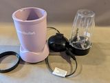 un mixeur rose posé sur une table à côté d'une tasse