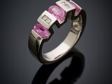 a close up of a pink sapphire and diamond ring on a black surface