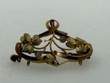a gold brooch with leaves on it on a white surface