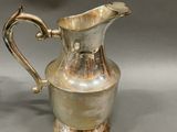 a silver pitcher sitting on a table next to a silver vase