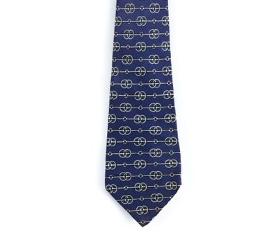 La cravate est bleue et dorée, avec un motif de cercles.