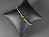 a black pillow with a gold beaded bracelet on it