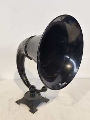 un vieux cor noir posé sur un support métallique, sur une surface blanche