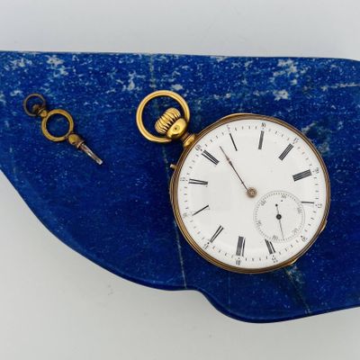 une montre de poche en or posée sur une pierre bleue