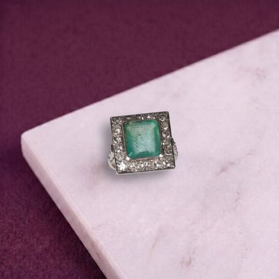 une image représentant une bague sertie d'une pierre verte posée sur une surface en marbre blanc