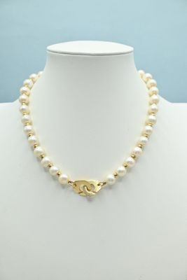 a white pearl necklace with a gold clasp on a mannequin
