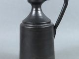 un vase noir muni d'une anse, posé sur une table