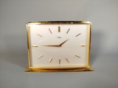 une horloge dorée avec un cadran blanc posée sur une table