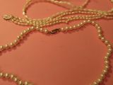 un collier de perles blanches muni d'un fermoir en or, posé sur une table rose