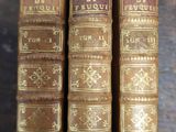 three old books sitting on top of a wooden shelf next to each other