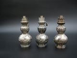 trois vases en argent posés sur une table, sur fond noir
