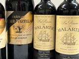 four bottles of red wine are lined up on a white surface