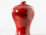 un vase rouge posé sur une surface blanche