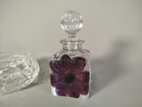 a glass bottle with a purple flower on it next to a glass bowl