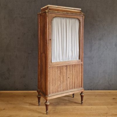 une vieille armoire en bois surmontée de rideaux, posée sur un parquet