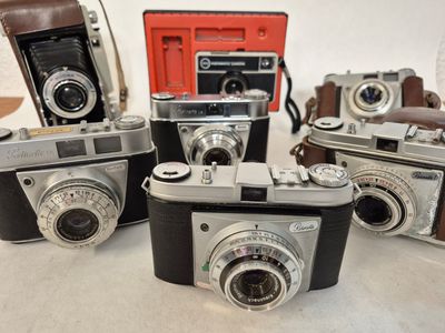 several old cameras are lined up on a table with a red case