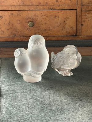two glass birds sitting on top of a table next to a dresser
