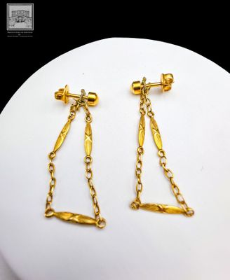 paire de boucles d'oreilles plaquées or avec des chaînes, présentées sur un plateau blanc