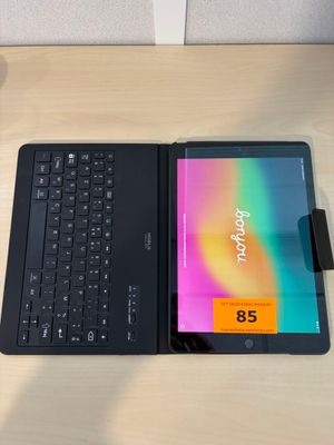 une tablette avec un clavier posée sur un bureau, à côté d'une tasse de café