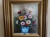 un tableau représentant des fleurs dans un vase bleu, accroché au mur