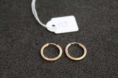 deux petites boucles d'oreilles en or en forme d'anneau posées sur une surface noire, avec une étiquette de prix
