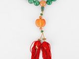 un collier composé de perles vertes et orange, orné d'un pompon