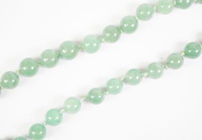 un gros plan sur un collier de perles de jade vert posé sur une surface blanche