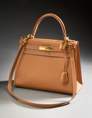 a brown leather handbag with gold hardware on a grey background