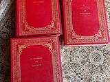 trois livres rouges posés sur un tapis, lui-même posé sur une table en bois