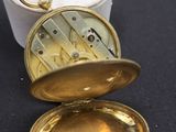 une petite montre de poche en or posée sur une surface noire
