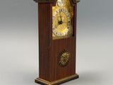 une petite horloge en bois avec un cadran doré sur fond gris
