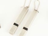 two silver and black earrings on a white surface next to a pair of scissors
