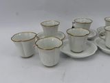 six white cups and saucers with gold rims on a white table